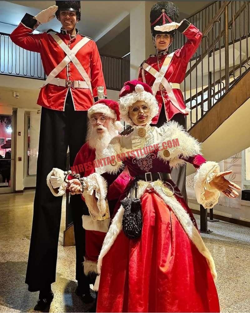 Corporate Santa for a Port St. Lucie office party: Santa, Mrs. Claus and two nutcracker soldiers on stilts indoors.