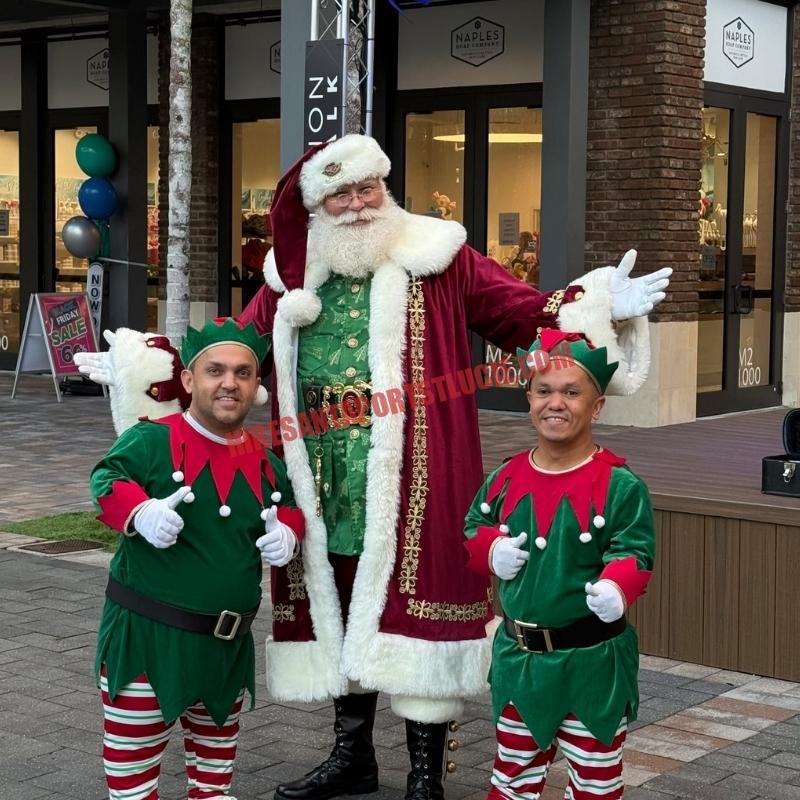 Santa Claus impersonator for hire in Port St. Lucie in a burgundy coat with two elves giving a thumbs-up.