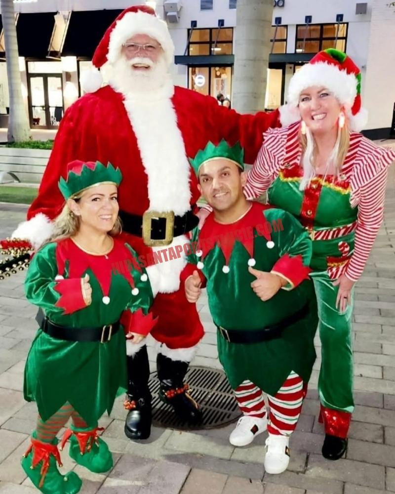 Santa for hire in Palm City, FL with three elves at dusk in front of string lights.